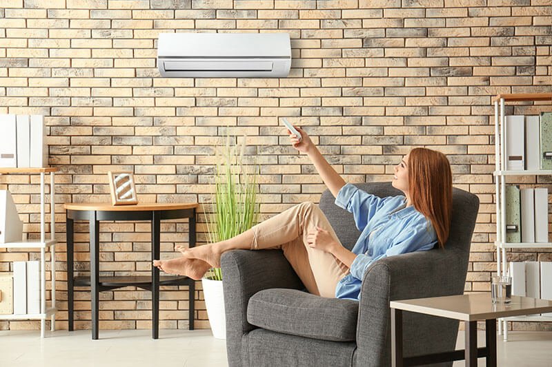 Woman sitting on a chair pointing a remote at a mini-split on the wall